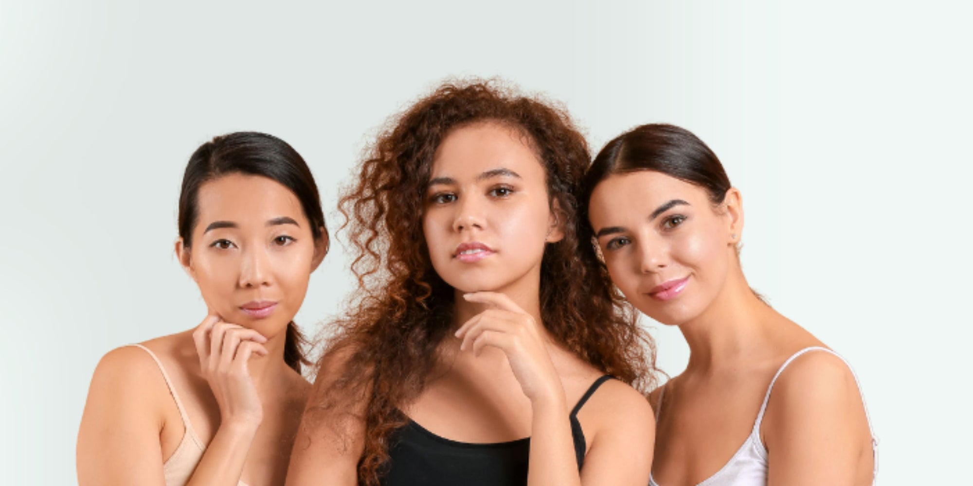 Three women with different hairstyles and skin tones standing together against a light gray background