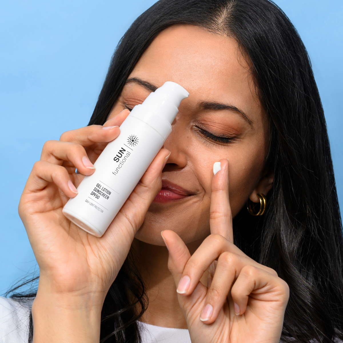 Woman applying sunscreen spray to her face against a blue background