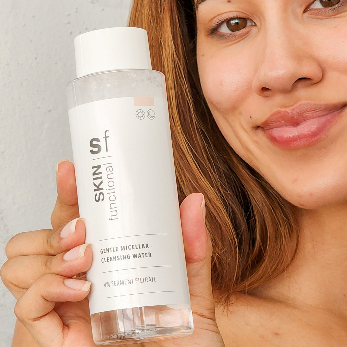 Woman holding a bottle of Skin Functional Gentle Micellar Cleansing Water against a neutral background
