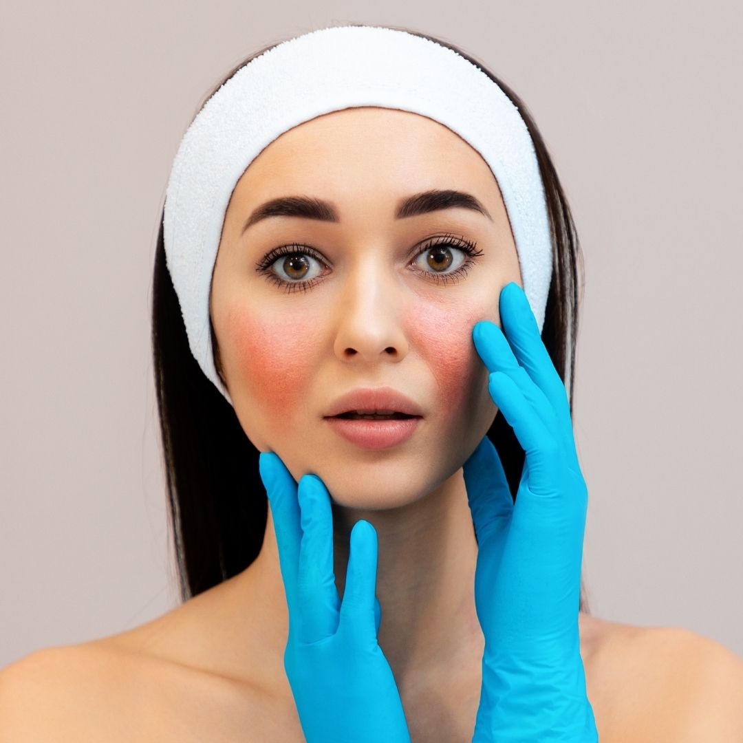 Woman wearing a white headband and blue gloves touching her face against a neutral background